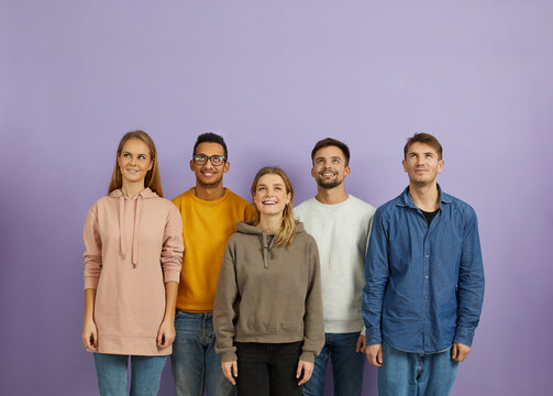 Happy Diverse Multiethnic Young People Isolated On Violet Studio Background Look Up At Sale Deal Or Promotion. Smiling Millennial Group Or Team Think Of Discount Or Offer. Copy Space, Advertising.