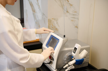 Close-up of the hand of a cosmetologist adjusting the program and functions on the monitor of modern medical equipment for cosmetology