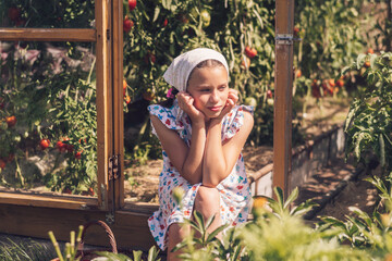 A girl in a summer dress and a kerchief enjoys the summer sun on the threshold of a...