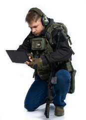 Fototapeta premium soldier, airsoft player in full gear works on a laptop in combat conditions. a man in headphones, a bulletproof vest, with a backpack and a belt, speaks, transmits information. White background.