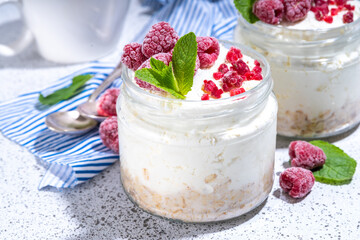 Overnight cheesecake oatmeal. Cheesecake morning breakfast layered parfafait dessert with homemade cottage cheese, mascarpone, oats and fresh raspberries, on sunny white concrete background copy space
