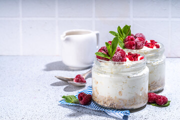 Overnight cheesecake oatmeal. Cheesecake morning breakfast layered parfafait dessert with homemade cottage cheese, mascarpone, oats and fresh raspberries, on sunny white concrete background copy space