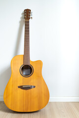 Fototapeta premium An acoustic dreadnought guitar leaned against the white wall background. Veritcal image copy space.