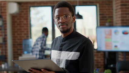 Fototapeta premium Portrait of african american man analyzing statistics on laptop, using computer to plan business development with financial charts. Male manager working on compnay growth. Handheld shot.