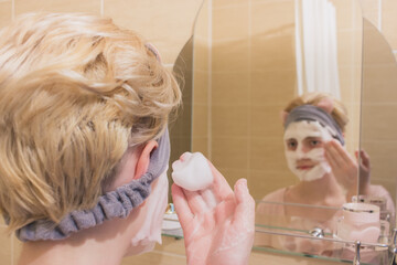 Teenager girl washing her face near mirror to prevent pubertal acne.