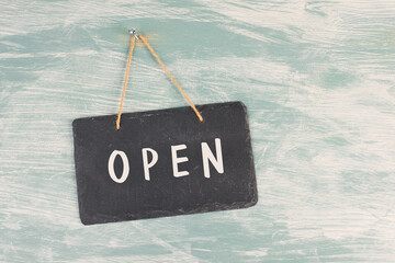 The word open is standing on a chalkboard sign, hanging on a blue textured weathered door, concept...