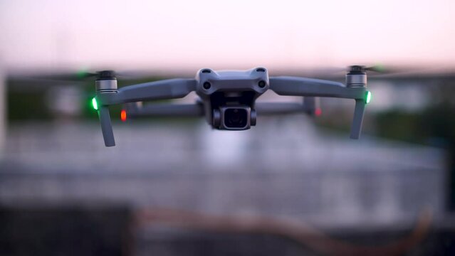 shot of grey drone with sensors and camera four propellors hovering at dusk with lights on, watermarks removed shot showing innovation and new technology