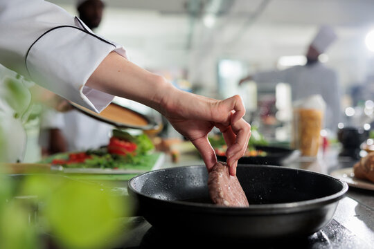 Close up of master chef hands cooking beef patty in hot pan while cooking gourmet dish for dinner service. Head cook frying minced meat in restaurant professional kitchen.