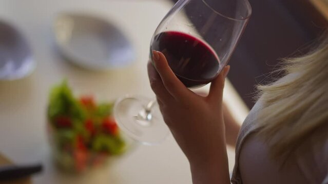 Woman makes tasty salad for dinner at table in light spacious kitchen at home focus on hand with wineglass extreme close view slow motion