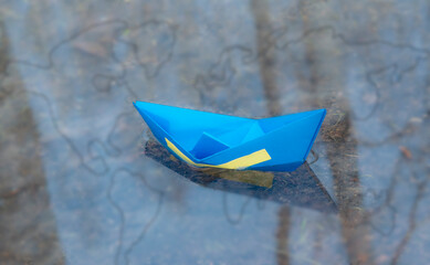 A paper boat in the color of the Flag of Ukraine floats on the water. National Emblem. The concept of freedom and independence of Ukraine in the world