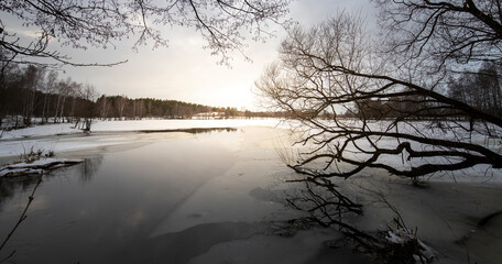 Epic spring landscape by the river. March evening, snow melts. Winding river with snow-covered banks and ice. Trees are reflected in the water.