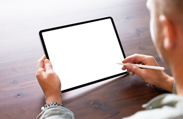Man using tablet computer with stylus pen, empty white screen mockup, over the shoulder view