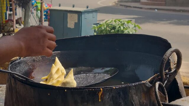close up of shop cook placing samosa potato filled flour hot pockets on strainer before frying in boiling hot oil to make this favorite street food snack available across India
