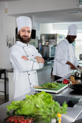Positive sous chef cutting fresh herbs to be used in gourmet cuisine dishes while looking at camera. Gastronomy expert wearing cooking uniform while preparing garnish for dinner service.