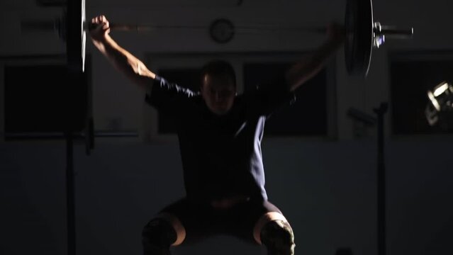 Sport. Weightlifting. The athlete deftly lifts the barbell with a heavy weight. Dark room