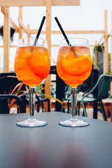 Two glasses of Aperol Spritz served on the terrace of modern bar. Popular Italian wine based cocktail and summer aperitif refreshing drink prepared with prosecco wine, bitter liqueur and soda water.