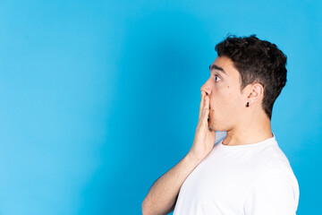 Side view of surprised hispanic teenager boy isolated on blue background.