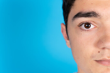 Fototapeta premium Half portrait of serious hispanic teenager boy looking at camera isolated on blue background.