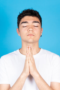 Believer And Devout Hispanic Teenager Boy Praying Isolated On Blue Background.