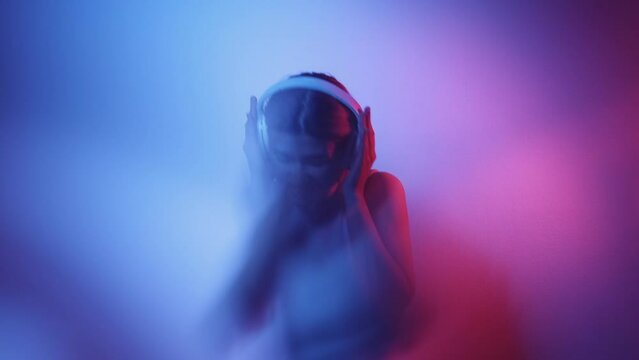 Music energy. Sound inspiration. Party fun. Defocused pink blue neon light amused girl enjoying dancing in headphones isolated on dark uv color gradient artistic out of focus.