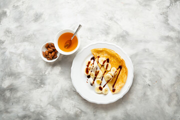 Overhead view of crepes banana honey syrup on plate light surface