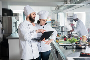 Sous chef with modern laptop recommending dinner dish service recipe to head chef. Gastronomy...