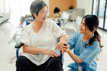 Asian nurse taking care and talking mature female patient sitting on wheelchair in hospital. Healthcare concept.