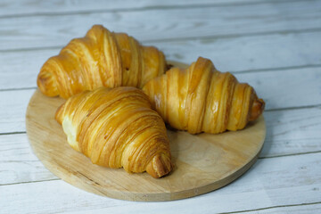 Fresh baked croissants on wooden cutting board on concrete grey surface in dark 