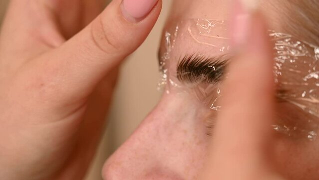 The master uses a plastic film during lamination of the eyebrows.