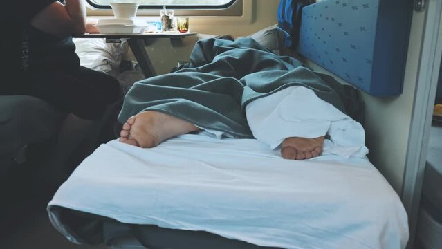 A young man is sleeping in a train carriage. Naked heels close-up.