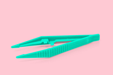 A green plastic sterile surgical tweezers isolated on pink background.