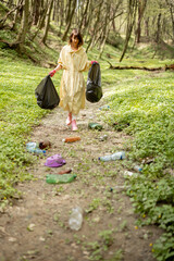 Young woman in protective clothes collecting scattered plastic garbage in the woods. Problem of bed...