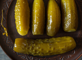 Salted pickled cucumbers on a brown plate on a wooden texture