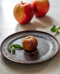 Baked apple on a brown plate with mint leaves and powdered sugar