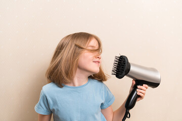 little girl dries her hair with a hair dryer with a comb attachment. hair care at home. simple...