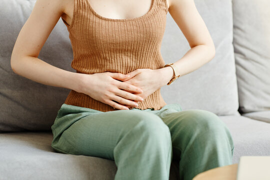 Minimal cropped shot of young woman suffering from cramps holding hands on stomach, copy space