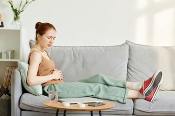 Side view portrait of young woman suffering from period cramps lying on couch, copy space