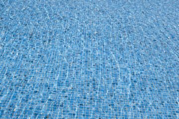 Clear surface water abstract background. Blue swimming pool reflecting the sun rippled. Pattern of the bottom of the pool made of rippled mosaic ceramic blue tiles.