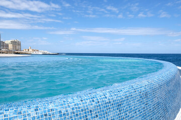 Blue clear water surface in swimming pool in a resort with sea views. Summer Vacation and rest concept. Luxury beach villa house. Blue tile mosaic pattern.