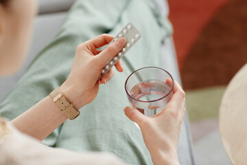 Close up of young woman taking birth control pills with glass of water, copy space