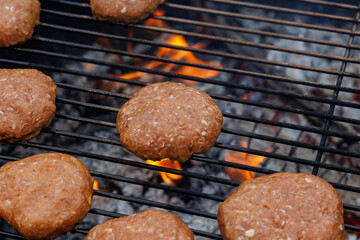 Homemade crispy fried hamburger patties on the grate of a charcoal grill over glowing coals with small flames