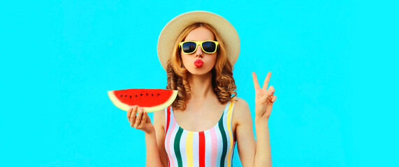 Summer portrait of stylish young woman blowing her lips with red lipstick with slice of watermelon wearing straw hat on blue background, blank copy space for advertising text