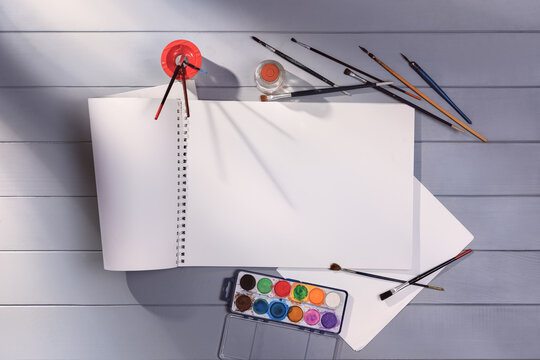 Drawing or painting in art studio top view. Blank paper mock-up on gray wooden table or floor background. Flat lay creative concept image with drawing and painting accessories