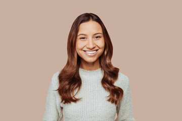 Fototapeta premium Close up portrait of young cheerful woman face, curly hair, wears green sweater, posing at studio on beige wall background. Female student. Copy space.