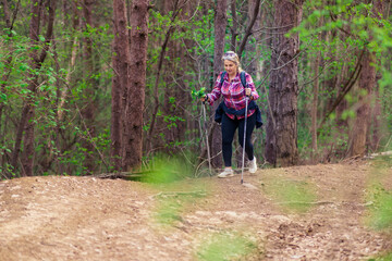 A mature woman in her 50s walks in the mountains. Use hiking poles.