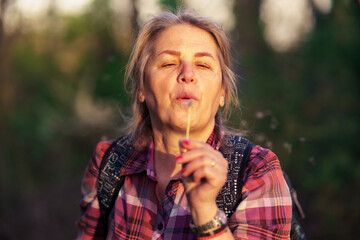 A portrait of a serious woman in her 50s who blows a dandelion to blow off his seeds.