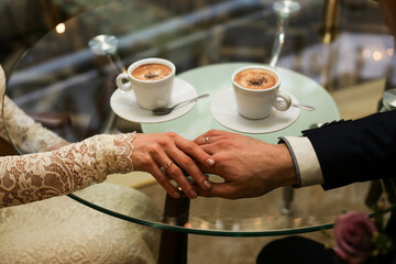 Fototapeta na wymiar Touching hands of groom and bride near two cups of coffee. Wedding day concept. Wedding picture. Love is, merry me today and every day.