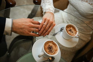 Touching hands of groom and bride near two cups of coffee. Wedding day concept. Wedding picture. Love is.