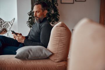 Side view of man sitting in comfortable armchair while typing on his phone in office space