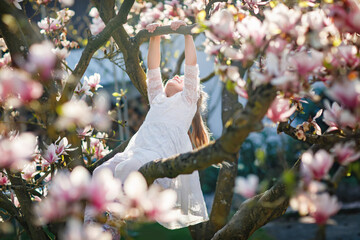 Cute spring fashion preschool girl under blossom magnolia tree. Little happy child and spring. Kid...